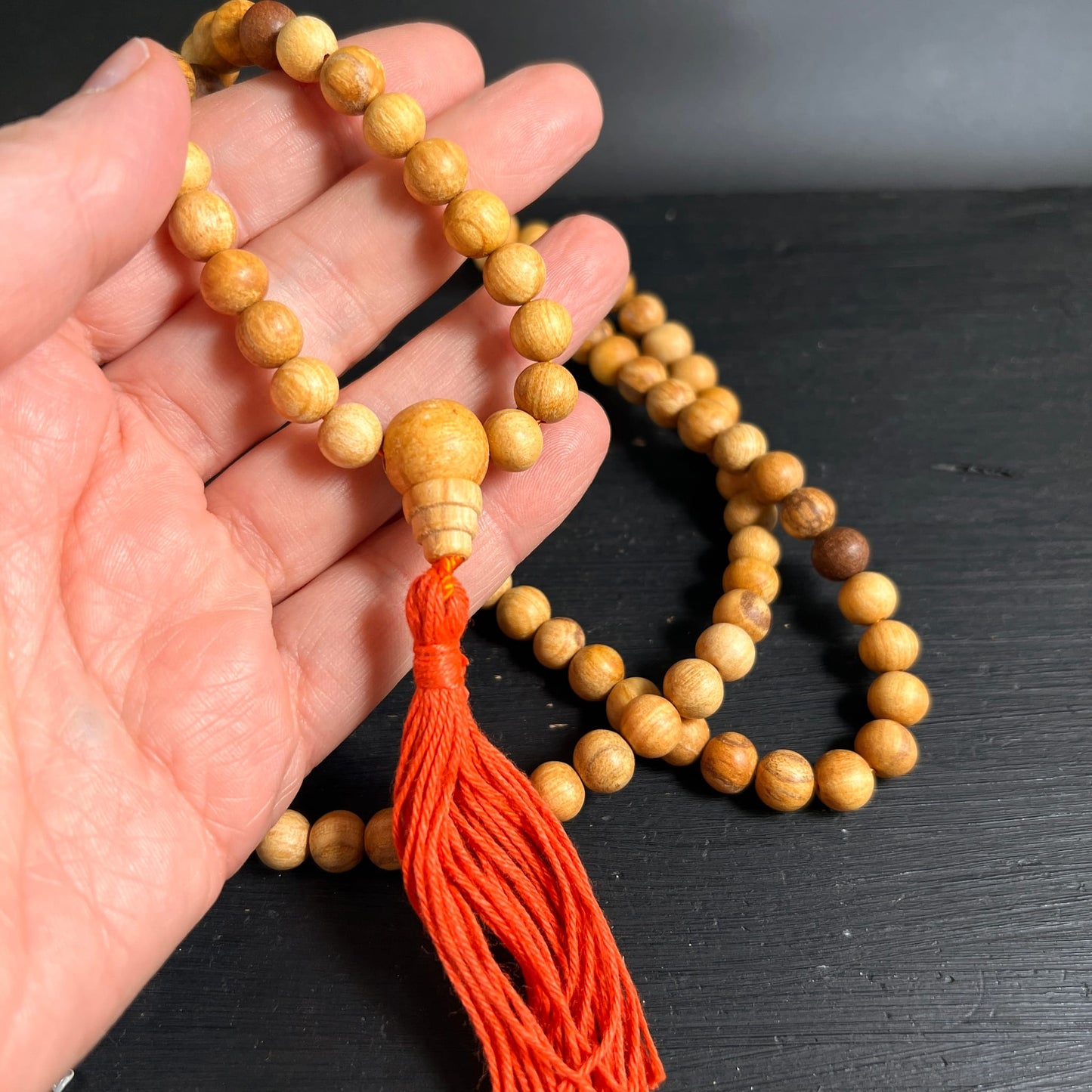 Palo Santo Mala | Nahaufnahme Guru-Bead | orange-rote Quaste | warmes Holz | auf Handfläche | Happy Minerals
