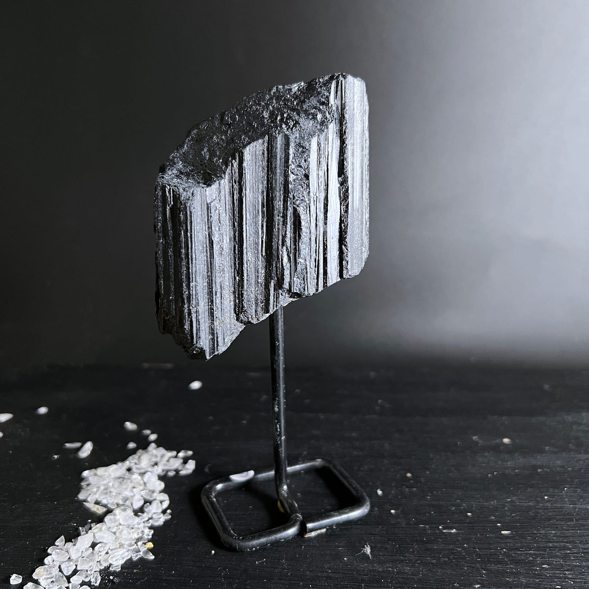 Schwarzer Turmalin Rohstein mit deutlicher Faserstruktur und metallischem Glanz auf Metallständer | Happy Minerals