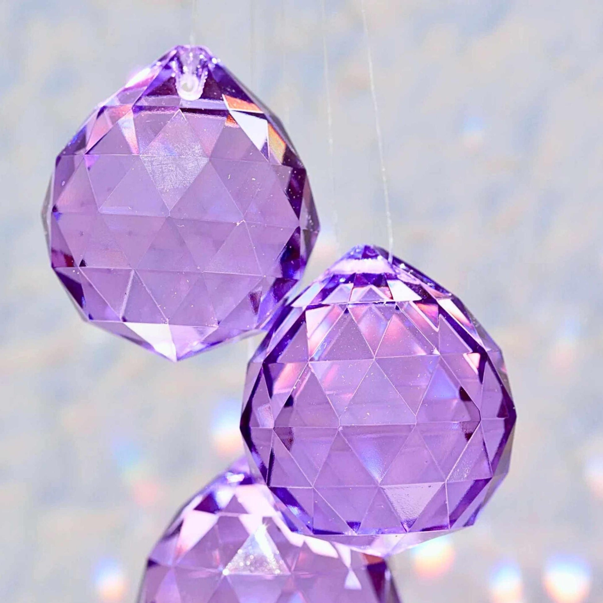 Lila Kristall-Sonnenfänger hängt im Fenster und wirft violette Lichtreflexe | Happy Minerals
