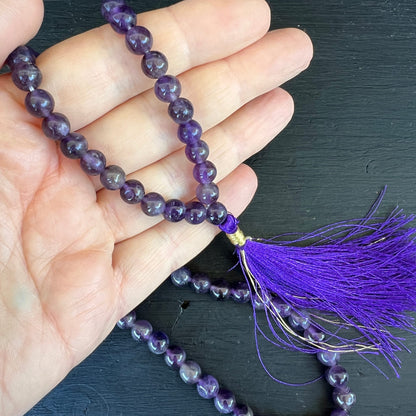 Amethyst Mala 108 Perlen | Nahaufnahme Quaste | violette Seide | Goldakzente | Hand hält | Happy Minerals