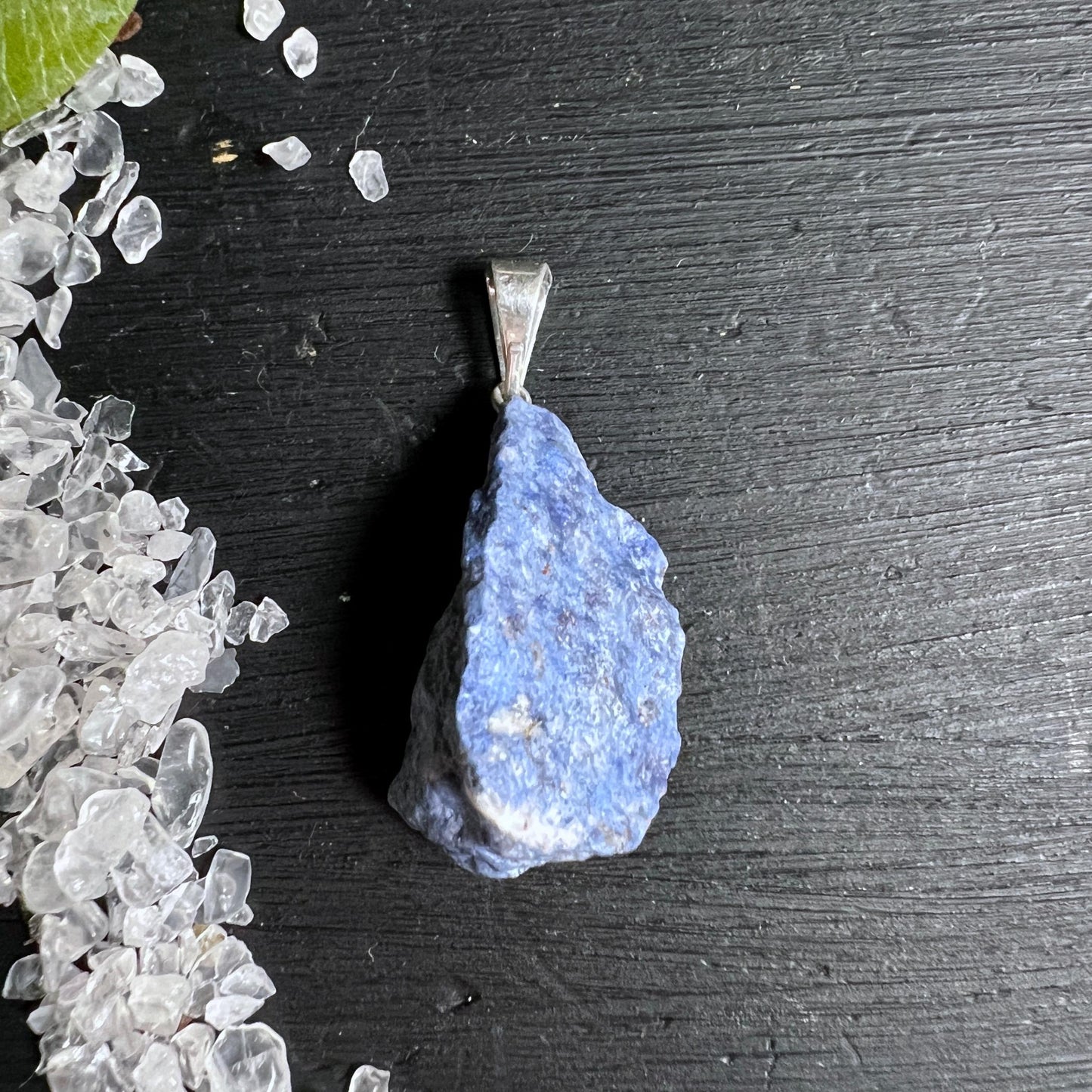 Roher blauer Dumortierit Anhänger mit versilberter Öse auf dunklem Holz