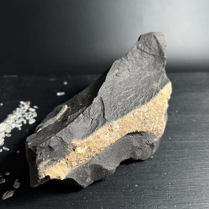 Roher dunkelgrauer Stein mit schroffer Bruchkante und beigem Sandsteinband quer durch die Mitte | Happy Minerals