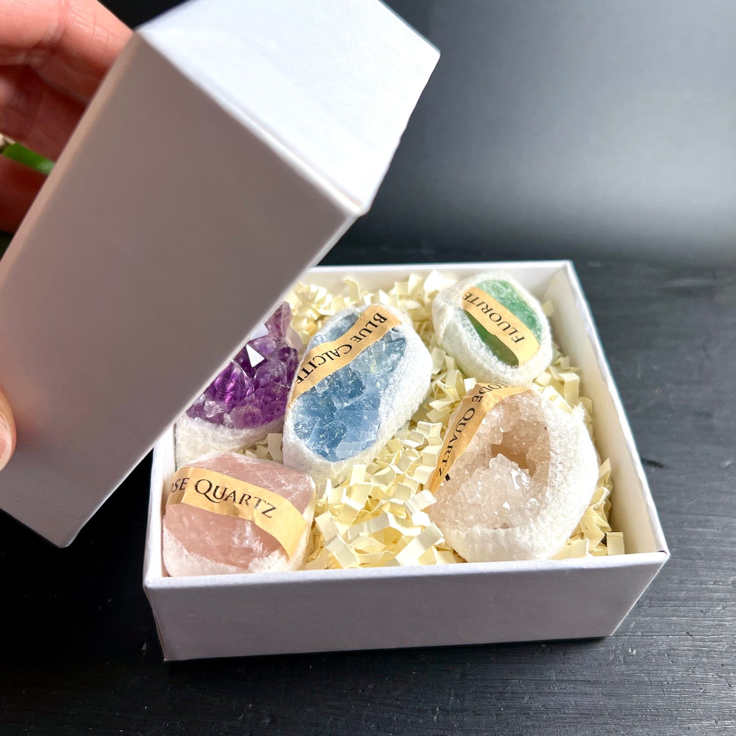 Hand öffnet weiße Geschenkbox | Amethyst Blauer Calcit Fluorit Bergkristall Geode | Strohfüllung | Happy Minerals