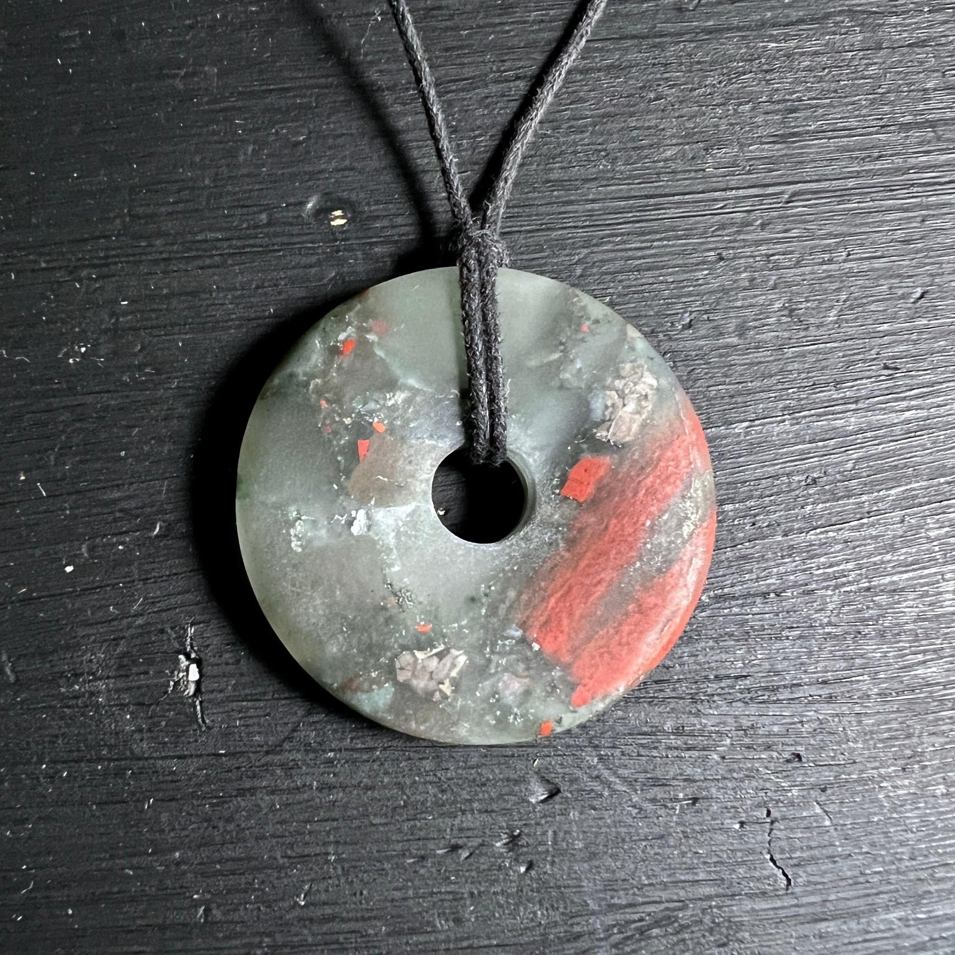 Heliotrop Donut Anhänger mit roten Jaspisadern auf schwarzem Holz.