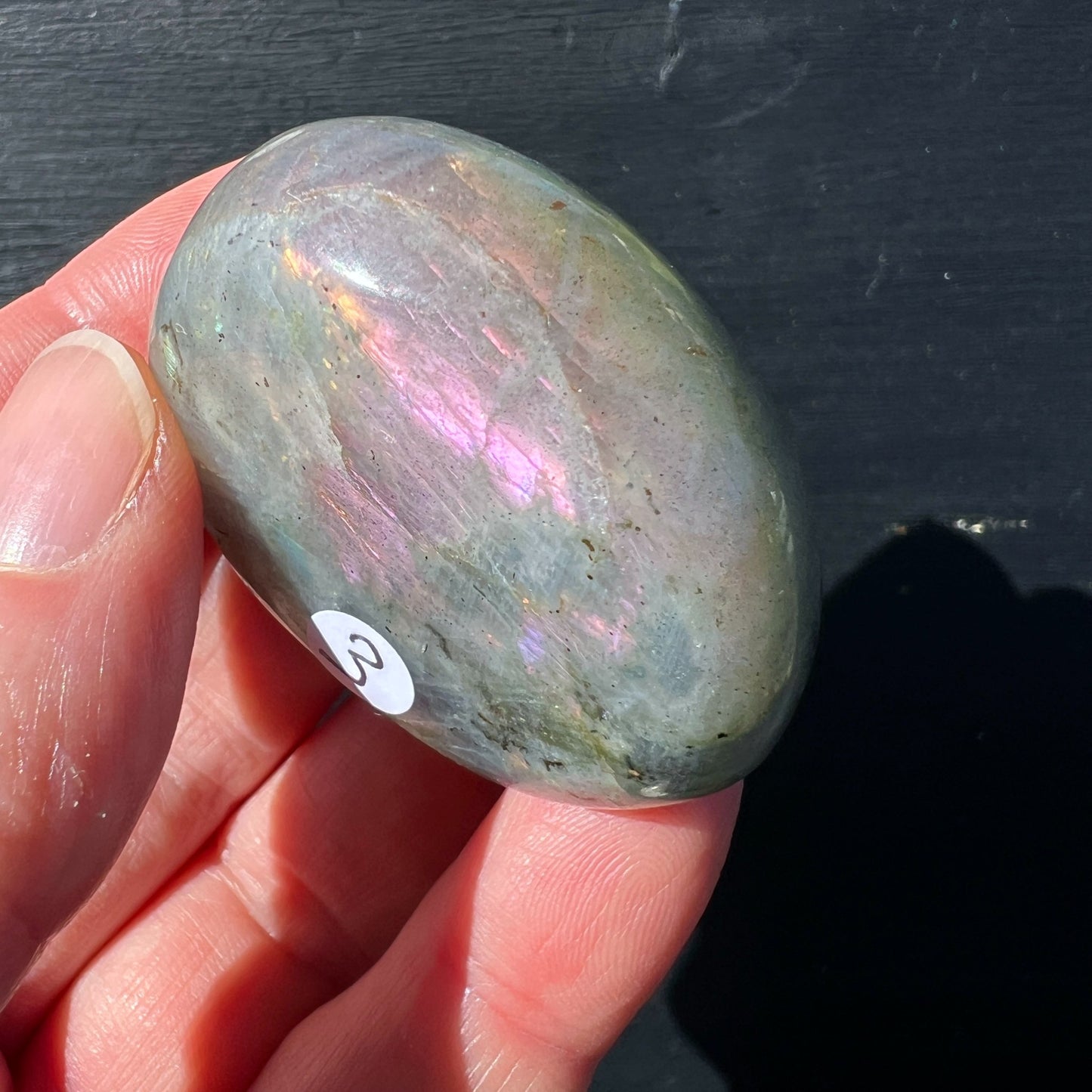Labradorit Handschmeichler oval grau mit rosa-goldenem Farbspiel in Hand gehalten | Happy Minerals