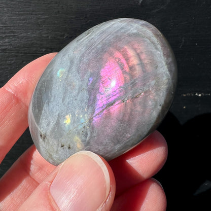Labradorit Handschmeichler mit rosa-violettem Farbspiel in der Hand gehalten | Happy Minerals