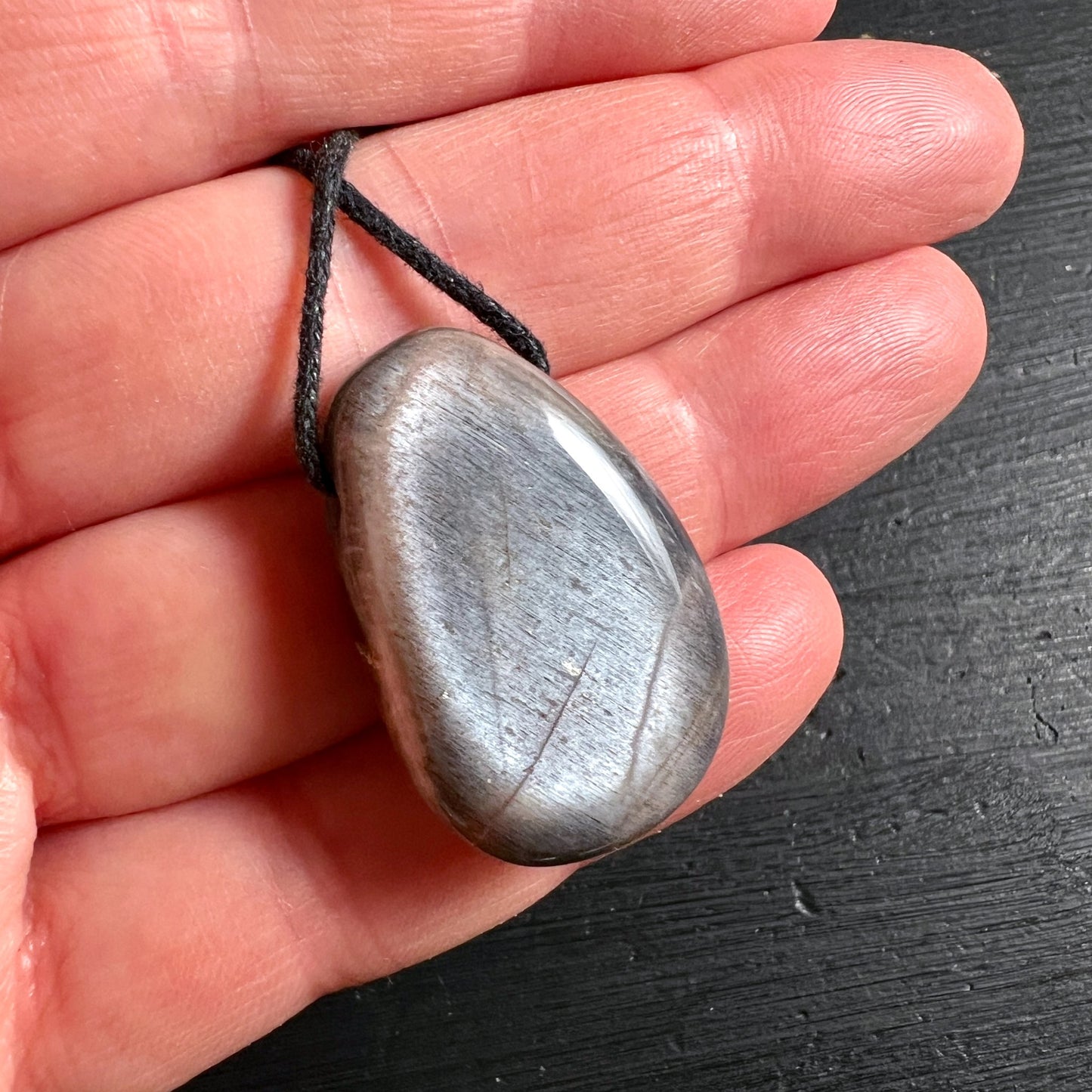 Grauer Mondstein Anhänger tropfenförmig 30mm mit schwarzer Kordel in Hand gehalten | Happy Minerals