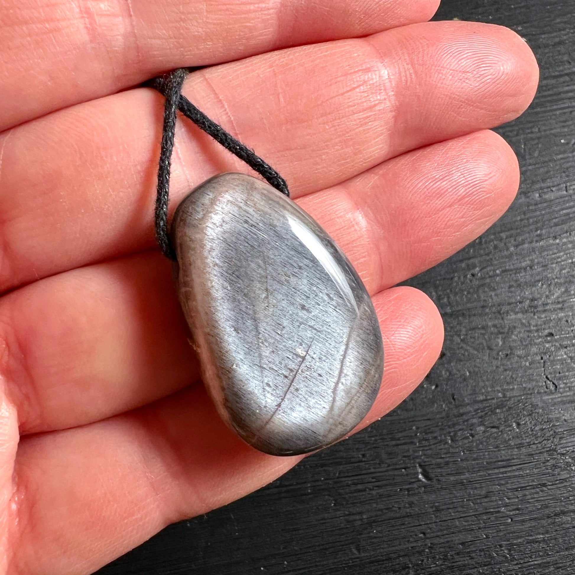 Grauer Mondstein Anhänger tropfenförmig 30mm mit schwarzer Kordel in Hand gehalten | Happy Minerals