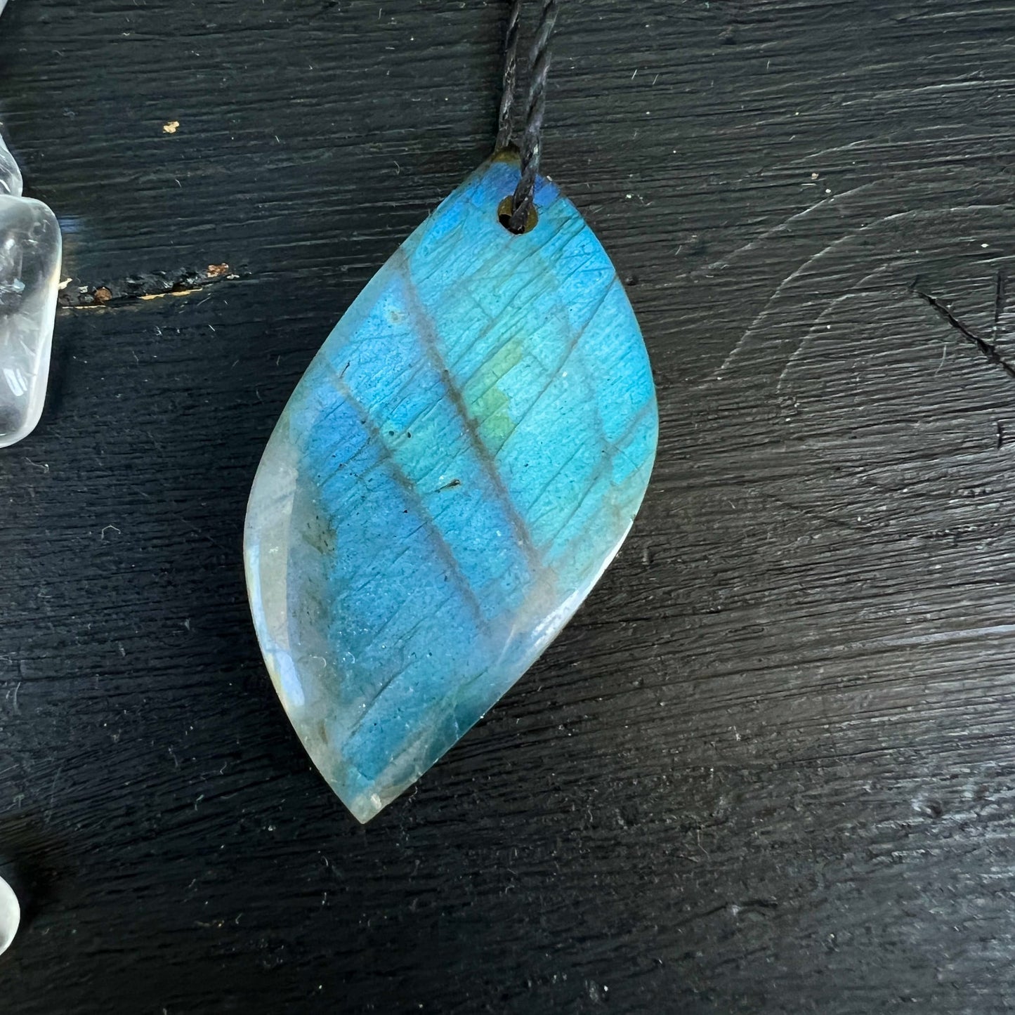 Labradorit Anhänger | leuchtendes Blau-Türkis | Blattform | schwarzes Band | dunkler Holzhintergrund | Happy Minerals