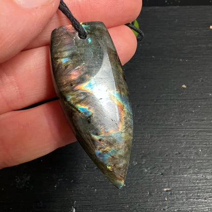 Labradorit Anhänger in Hornform, poliert, mit leuchtendem Orange-Blau-Lila Farbspiel auf dunkelgrauem Grund | Happy Minerals
