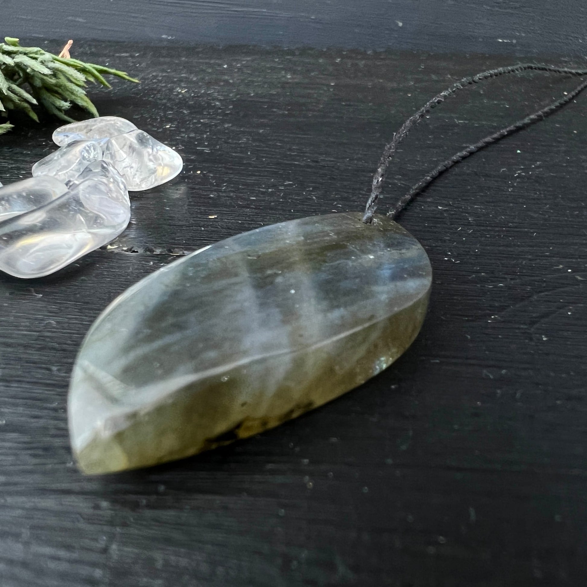 Labradorit Unikat | Rückseite grau-transparent | ovale Blattform | schwarzes Kordel | Kristalle im Hintergrund | Happy Minerals