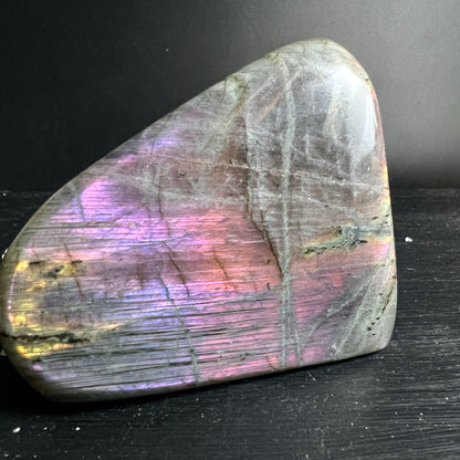 Labradorit Freiform mit violett-pinkem und goldenem Schiller auf grauem Untergrund, polierte Oberflaeche | Happy Minerals