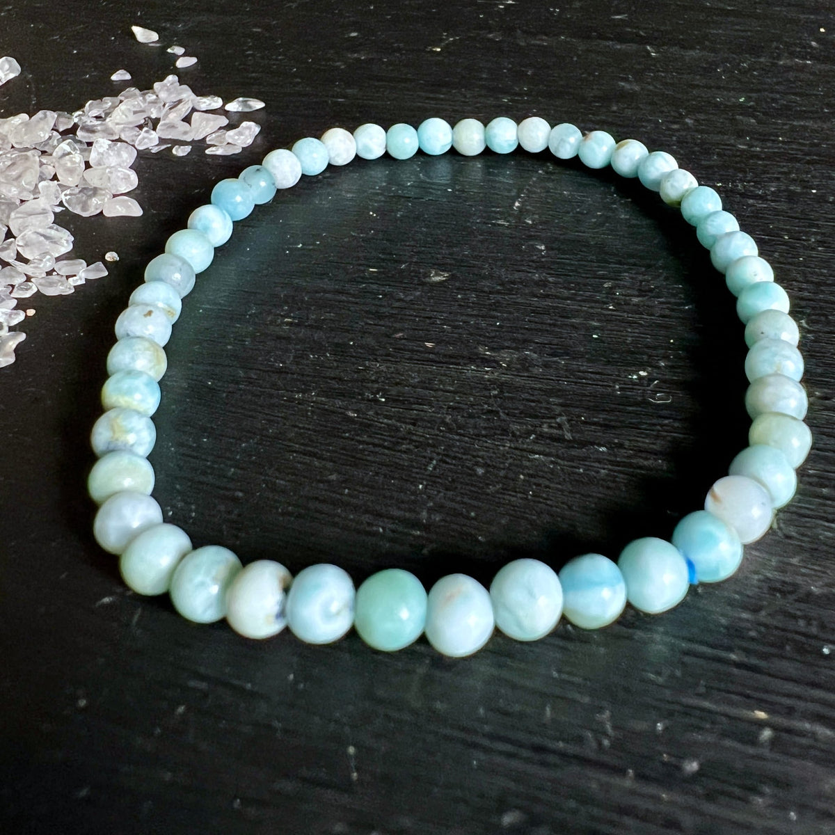 Larimar Armband aus runden Perlen in Hellblau und Cremeweiss mit wolkigen Marmor-Mustern, auf dunklem Holz | Happy Minerals