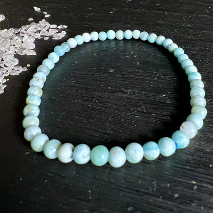 Larimar Armband aus runden Perlen in Hellblau und Cremeweiss mit wolkigen Marmor-Mustern, auf dunklem Holz | Happy Minerals