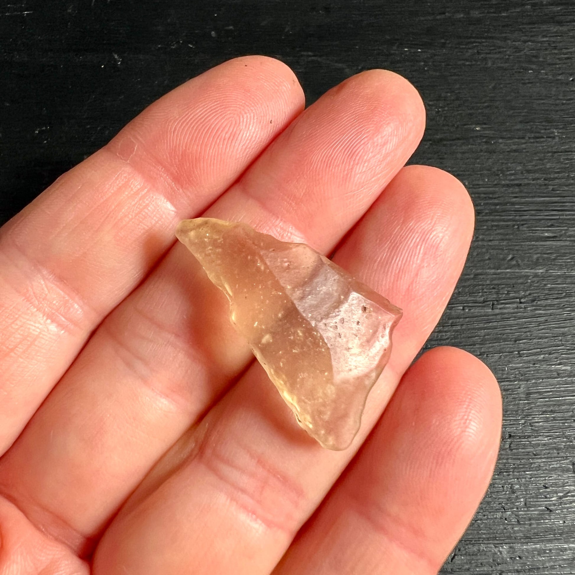 Libysches Wüstenglas Tektit, honigfarben-transparent mit splitteriger Kante, auf Fingern liegend | Happy Minerals