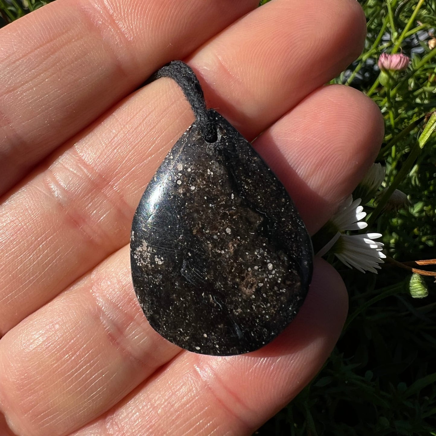 Mystischer Merlinit Tropfen | schwarz-braun | weiße Einschlüsse | auf Handfläche | Happy Minerals