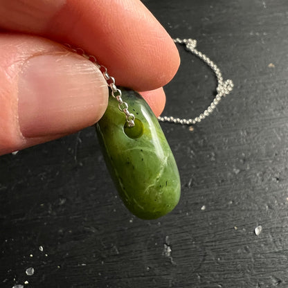 Nephrit Jade Kanada | Fingers halten Anhänger | Bohrloch sichtbar | schlanke Tropfenform | Silberkette | Happy Minerals