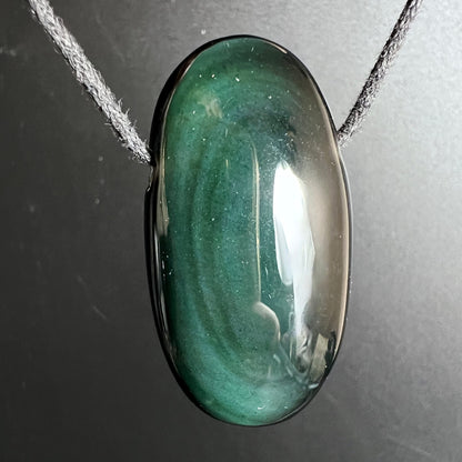 Ovaler Obsidian Anhaenger, smaragdgruen schimmernd mit dunklen Schlieren und silbrig glaenzender Oberflaeche | Happy Minerals