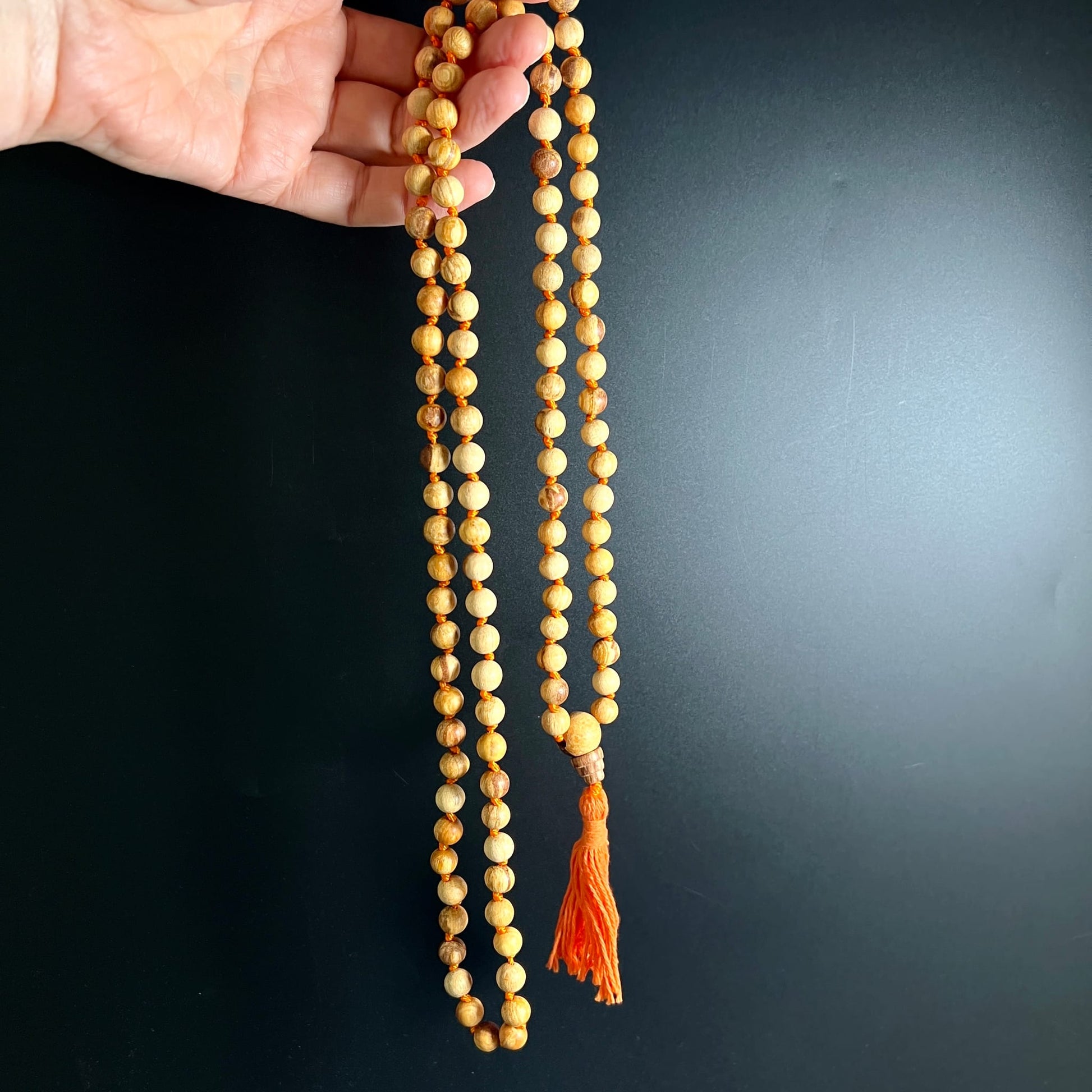 Palo Santo Mala | Hand hält geknotete Mala | warme Holzperlen | orangefarbene Quaste | Happy Minerals
