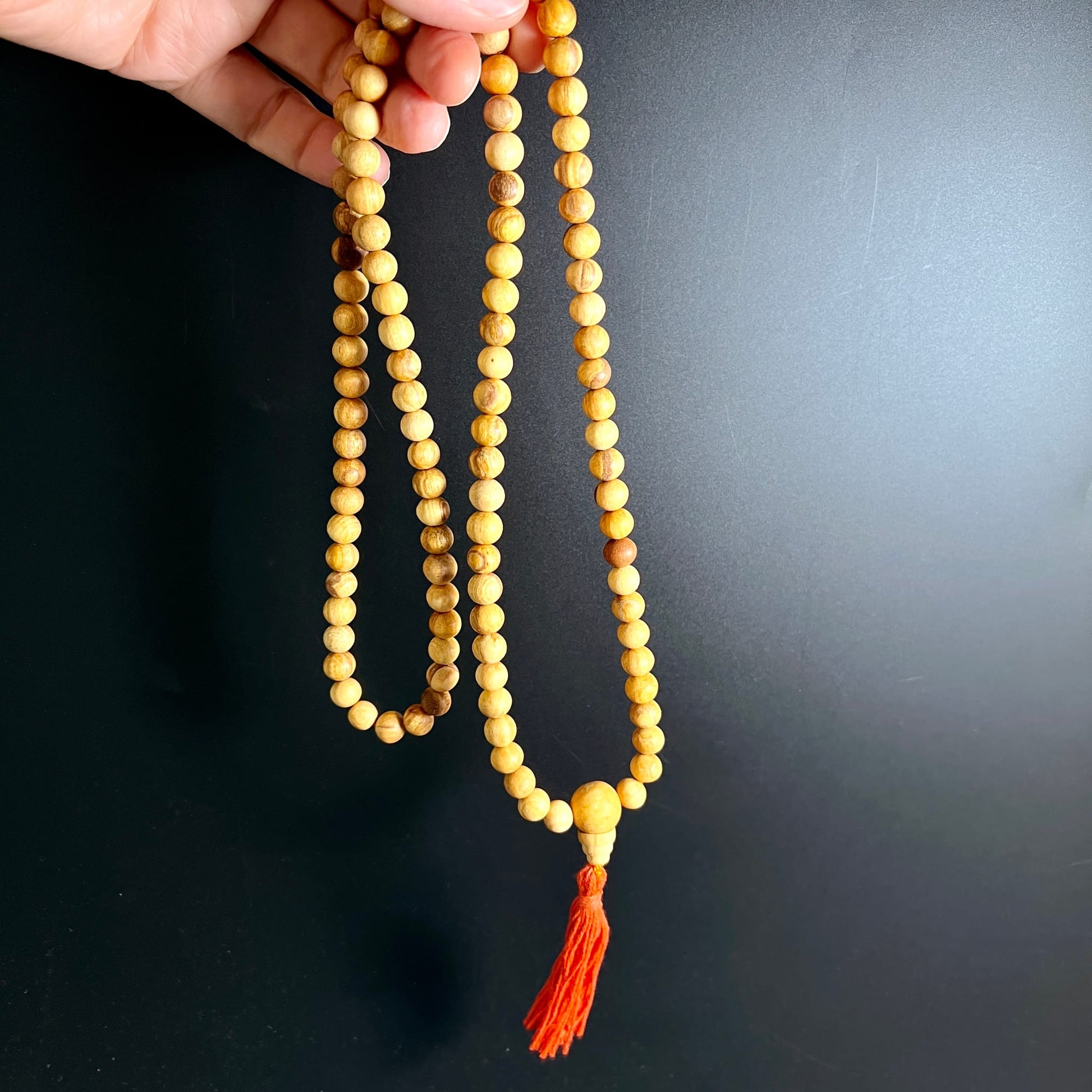 Palo Santo Mala | Hand hält Mala | hängend | warme Holzmaserung | leuchtend rote Quaste | Happy Minerals