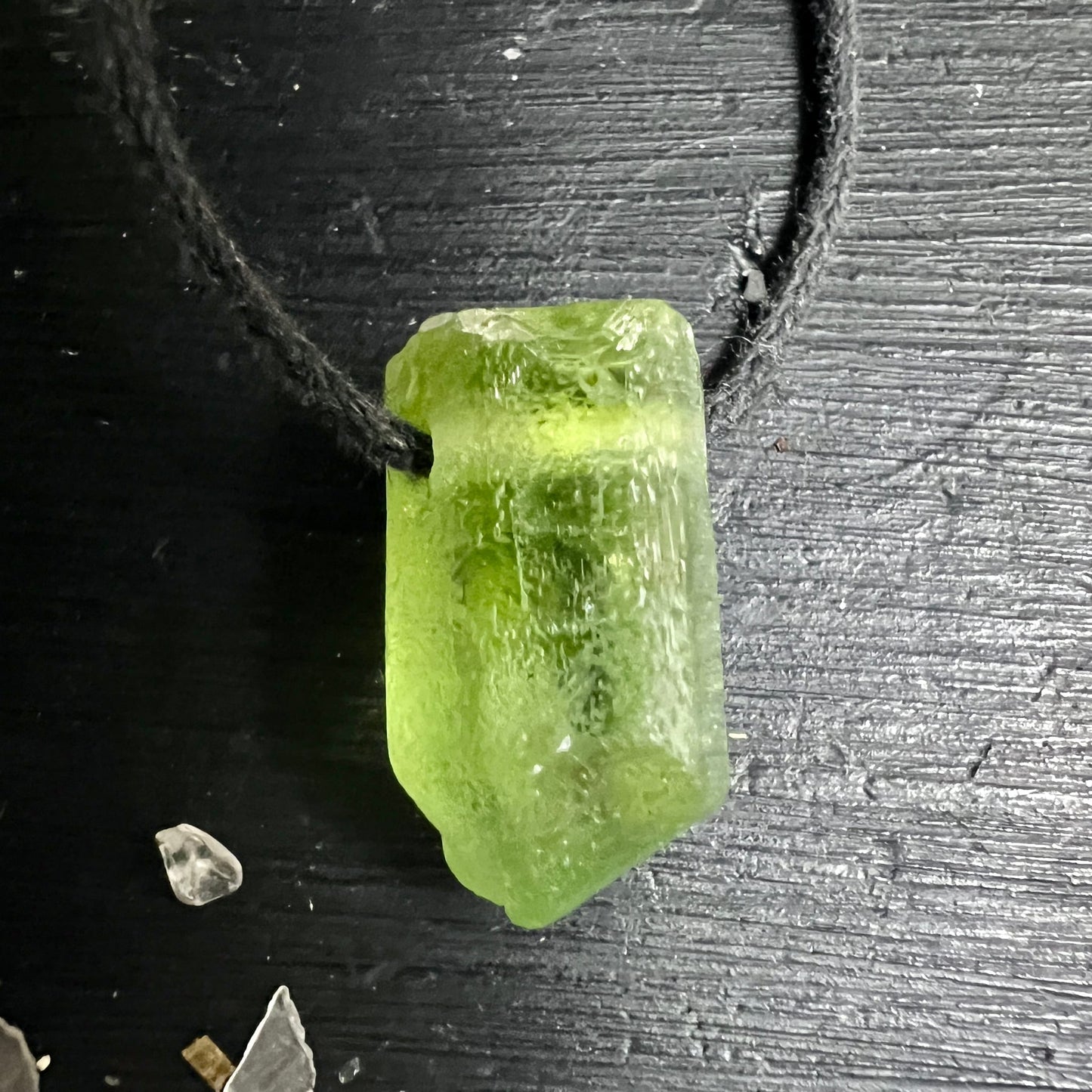 Peridot Rohstein olivgrün-transparent, blockige Rohform mit rauer Oberfläche, dunklen Einschlüssen, an schwarzer Kordel | Happy Minerals
