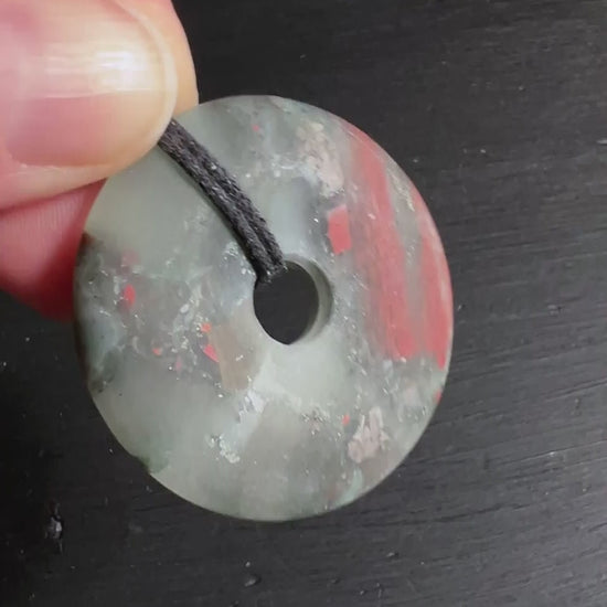 Heliotrop Donut Anhänger mit roten Jaspisadern und schwarzem Band.