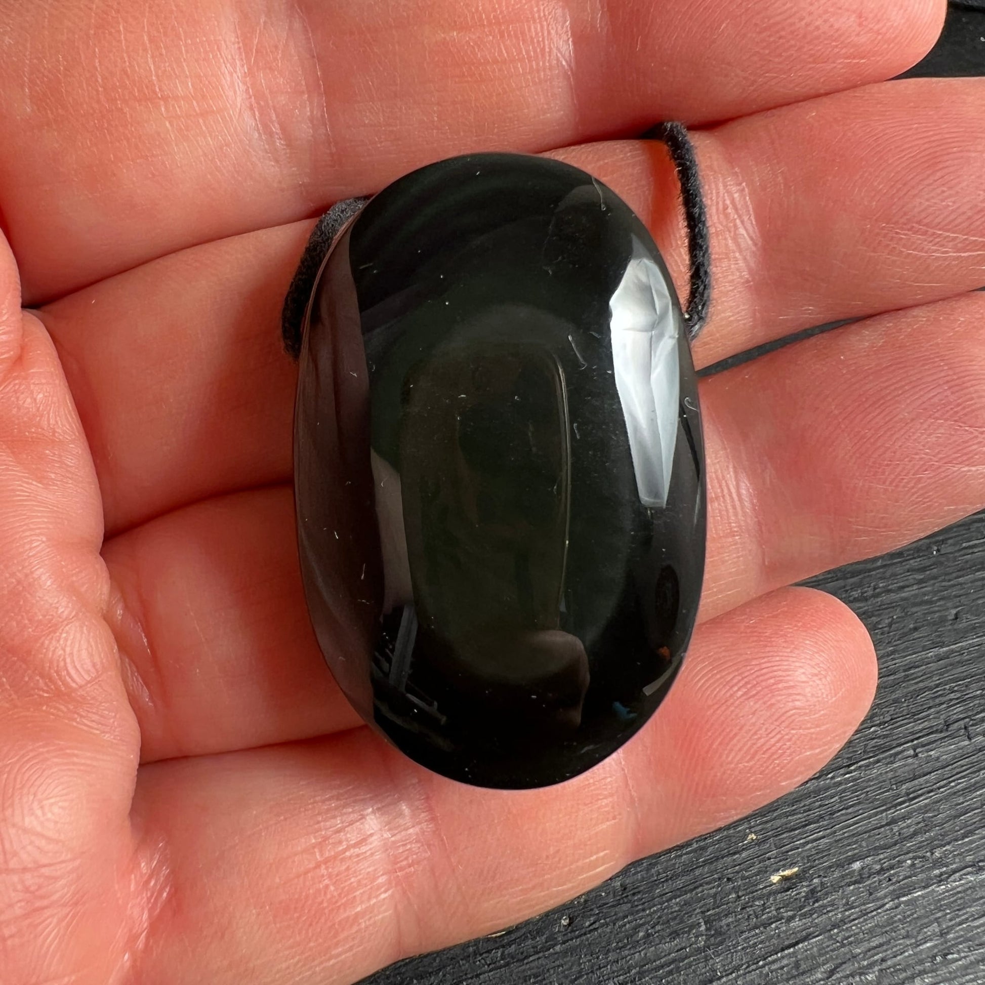 Regenbogenobsidian in der Hand | tiefschwarz glänzend | abgerundete Form | schwarzes Band | Happy Minerals