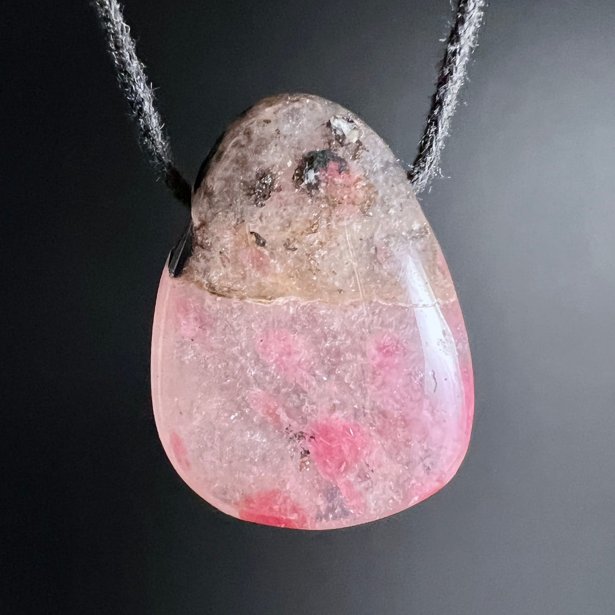 Rhodonit Anhänger in Tropfenform, oben grau-braun matt, unten rosa-pink glänzend mit dunklen Flecken | Happy Minerals