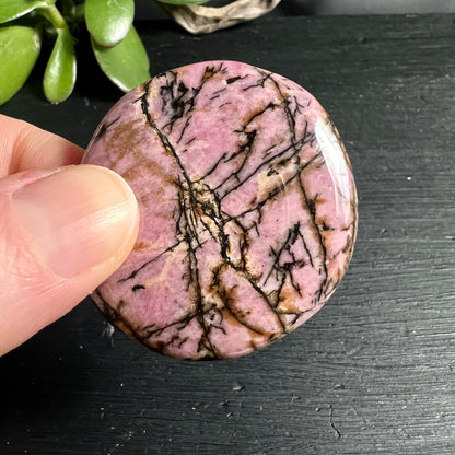 Rhodonit Handschmeichler | Hand zeigt Größe | rosa Grundfarbe | schwarze Maserung | Australien | Happy Minerals