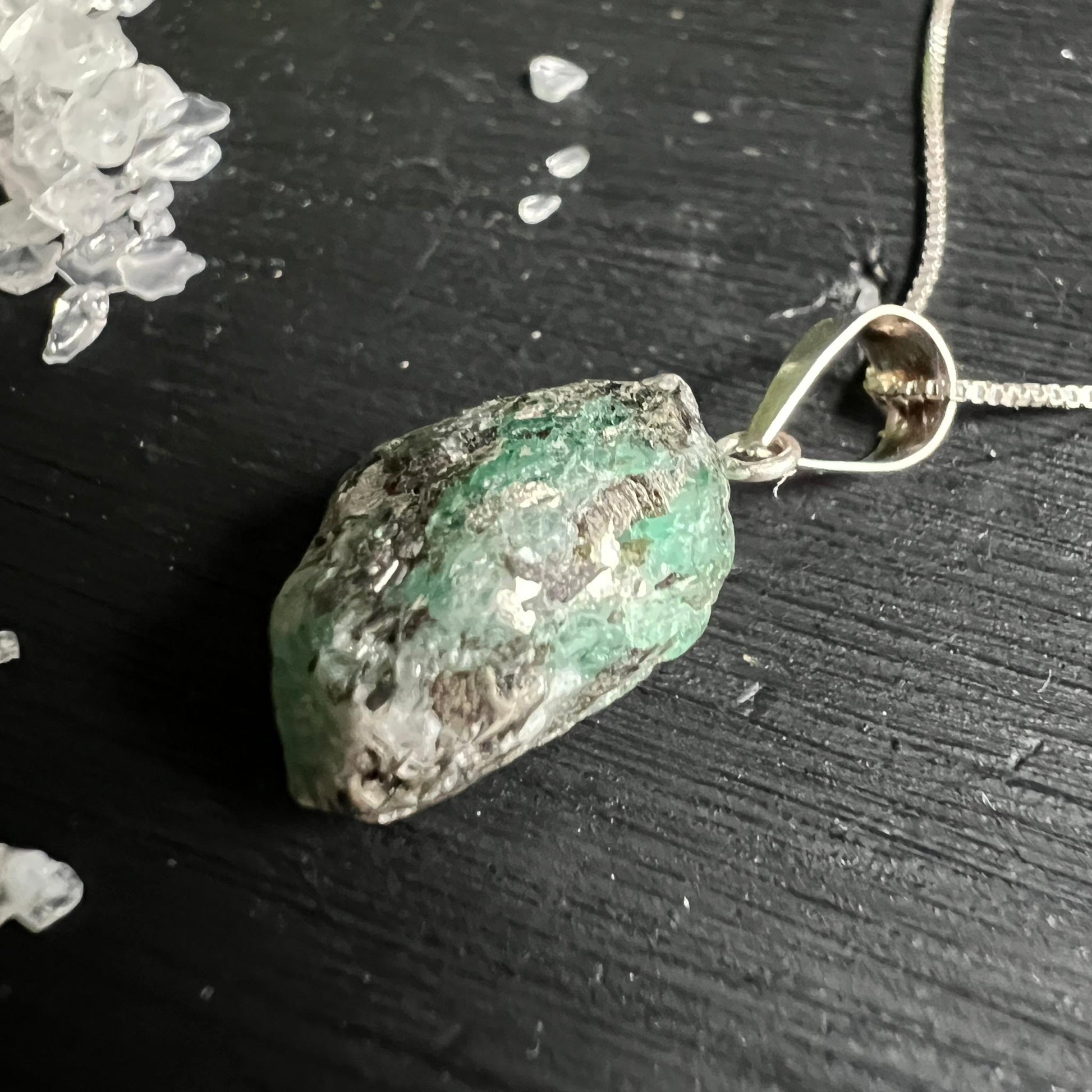 Roher gruener Smaragd Schmuck Anhaenger Draufsicht auf schwarzem Holz