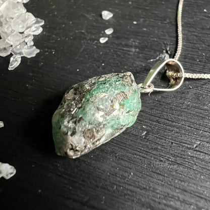 Roher gruener Smaragd Schmuck Anhaenger Draufsicht auf schwarzem Holz