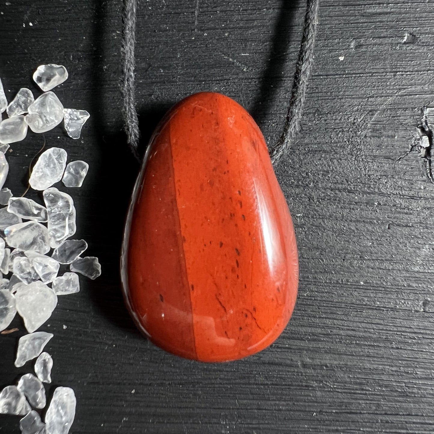 Roter Jaspis Anhaenger 28x18mm mit schwarzem Band auf dunklem Hintergrund