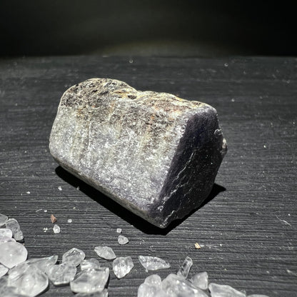 Roher Saphirstein mit grau-silbrig glimmernder Oberflaeche und dunkler kristalliner Bruchkante | Happy Minerals