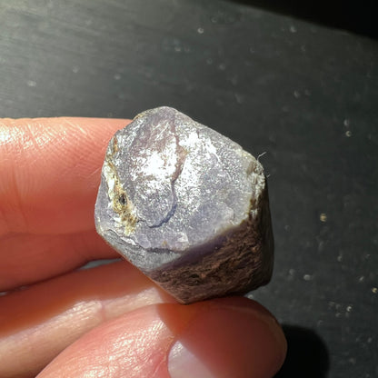 Roher Saphir Kristall mit grau-violetter Flaeche, metallischem Glanz und brauner Kruste, Sechseckform | Happy Minerals