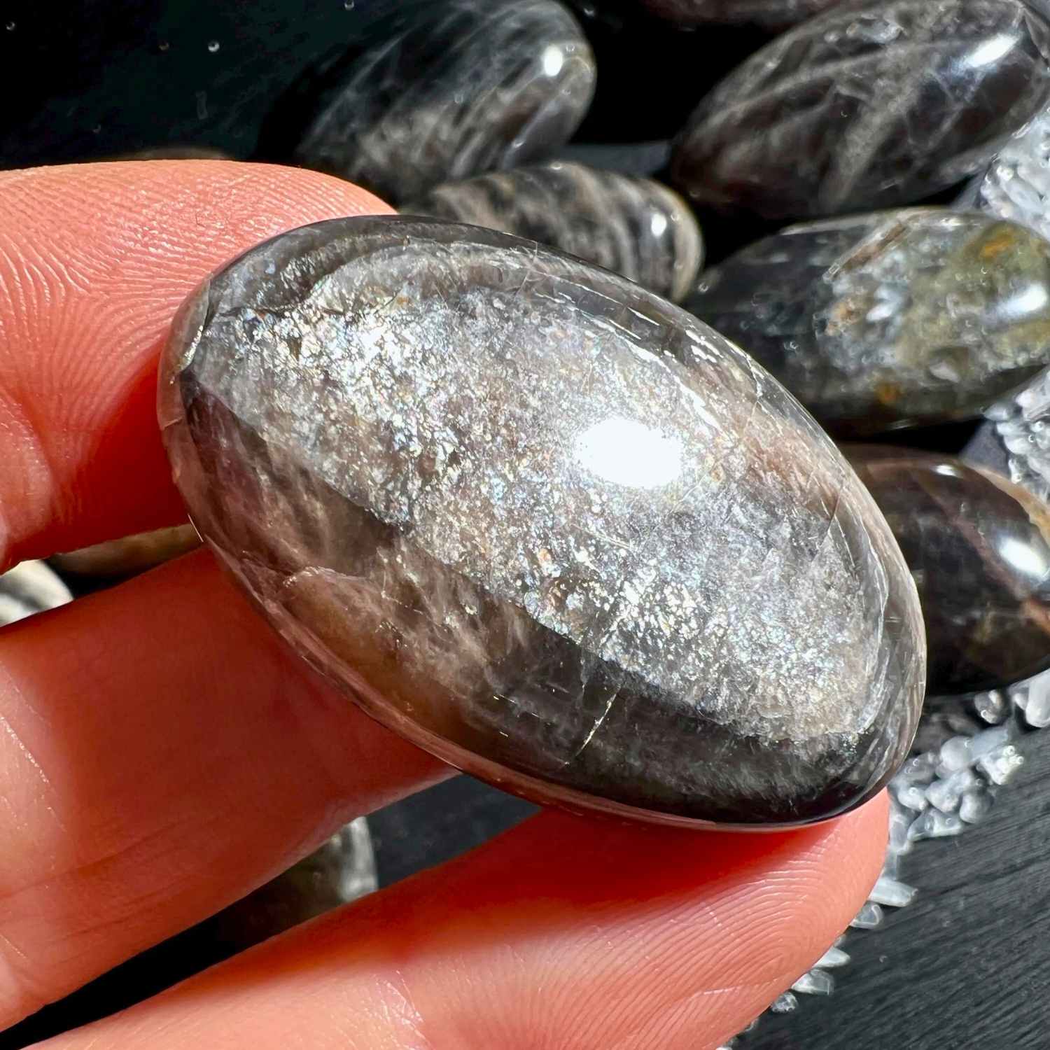 Schwarzer Mondstein Palm Stone in Hand mit silbernem Adulareszenz Schimmer