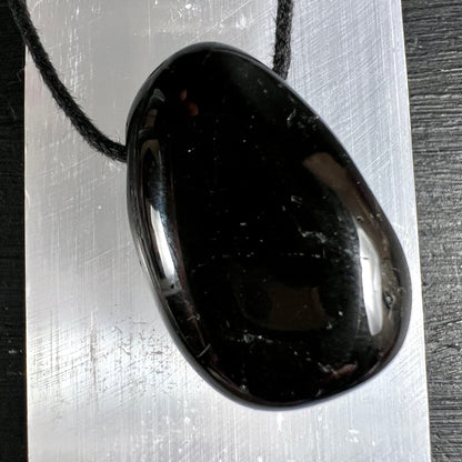 Schwarzer Turmalin Anhänger, oval poliert, tiefschwarz mit silbrigem Glanz, weisse Mineraleinschlüsse, schwarze Kordel | Happy Minerals