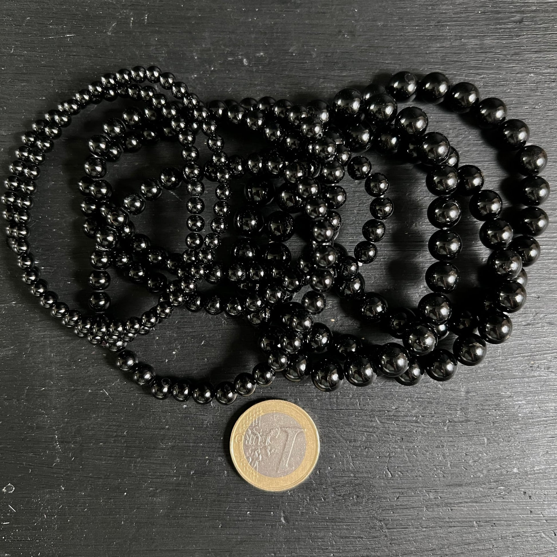 Mehrere schwarze Turmalin Armbänder mit hochglanzpolierten Kugelperlen 3–4mm, tiefschwarz ohne Einschlüsse, neben 1-Euro-Münze | Happy Minerals