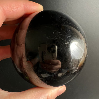 Schwarzer Turmalin Kugel 73mm, tiefschwarz glänzend mit silbrigen Ritzlinien, spiegelnde Oberfläche | Happy Minerals
