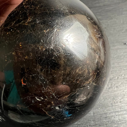 Schwarzer Turmalin Kugel 73mm, tiefschwarz mit goldbraunen Schlieren, weissen Rissen und seidigem Hochglanz | Happy Minerals
