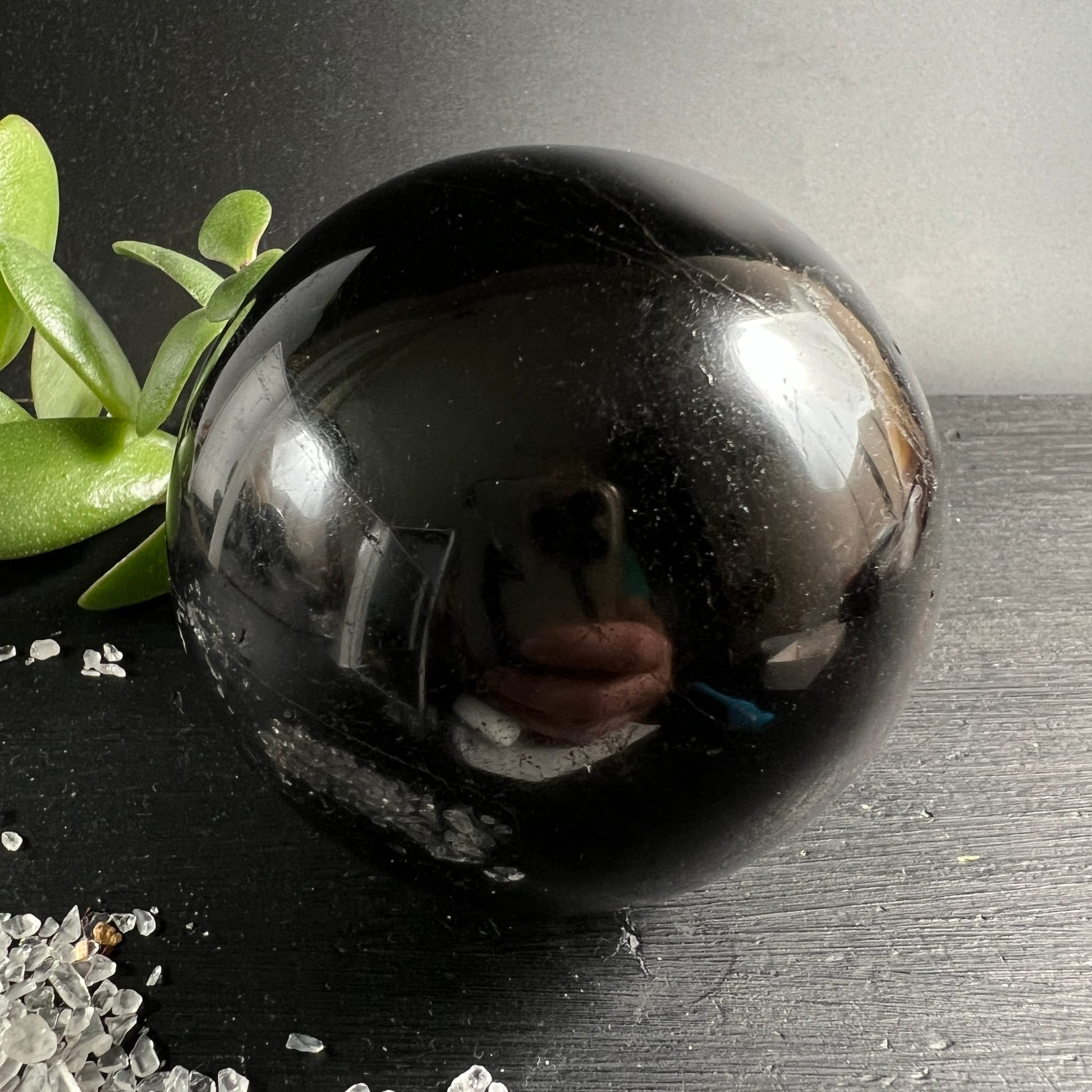 Schwarzer Turmalin Kugel 73mm, tiefschwarz glänzend mit feinen Kratzspuren, spiegelt Umgebung | Happy Minerals