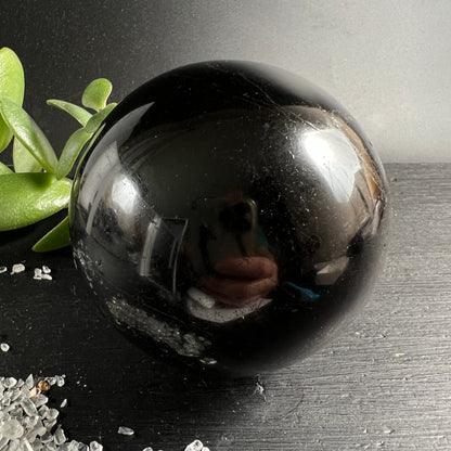 Schwarzer Turmalin Kugel 73mm, tiefschwarz glänzend mit feinen Kratzspuren, spiegelt Umgebung | Happy Minerals