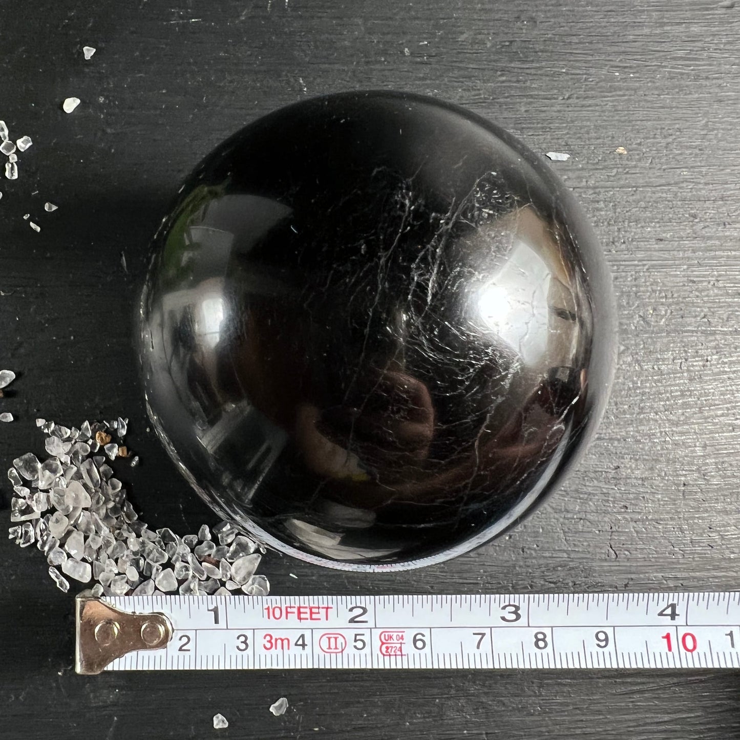 Schwarzer Turmalin Kugel von oben | Maßband zeigt ca. 9cm | weiße Äderung | Madagaskar | Happy Minerals