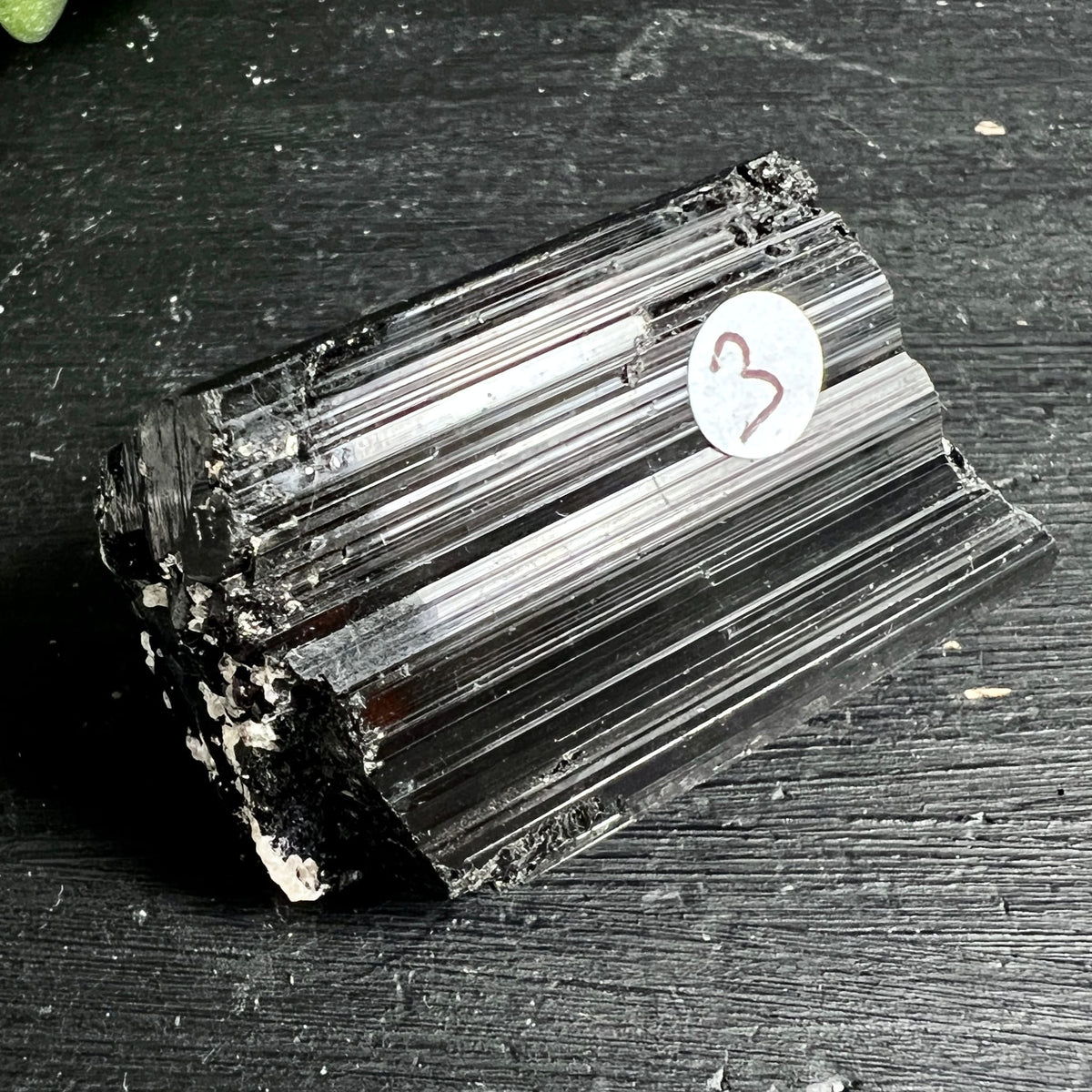 Schwarzer Turmalin Rohkristall mit tiefschwarzem Glanz, markanten vertikalen Rippen und weissen Mineraleinschlüssen | Happy Minerals