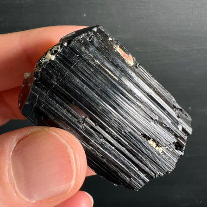Schwarzer Turmalin Rohkristall mit tiefen vertikalen Striemen, metallischem Glanz, weissen Feldspat-Einschlüssen und orangem Fleck | Happy Minerals