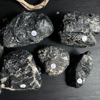 Fünf schwarze Turmalin Rohsteine aus Brasilien mit Quarz auf dunklem Untergrund