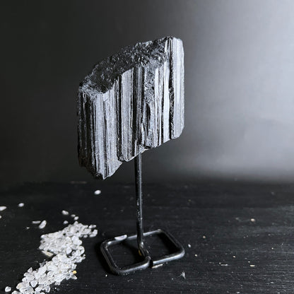 Schwarzer Turmalin Rohstein mit deutlicher Faserstruktur und metallischem Glanz auf Metallständer | Happy Minerals
