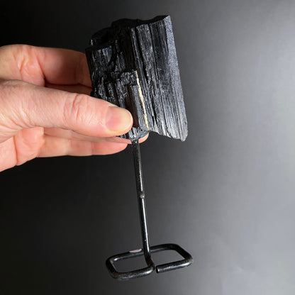 Schwarzer Turmalin Rohstein mit laengsrilliger Struktur auf schwarzem Metallständer | Happy Minerals