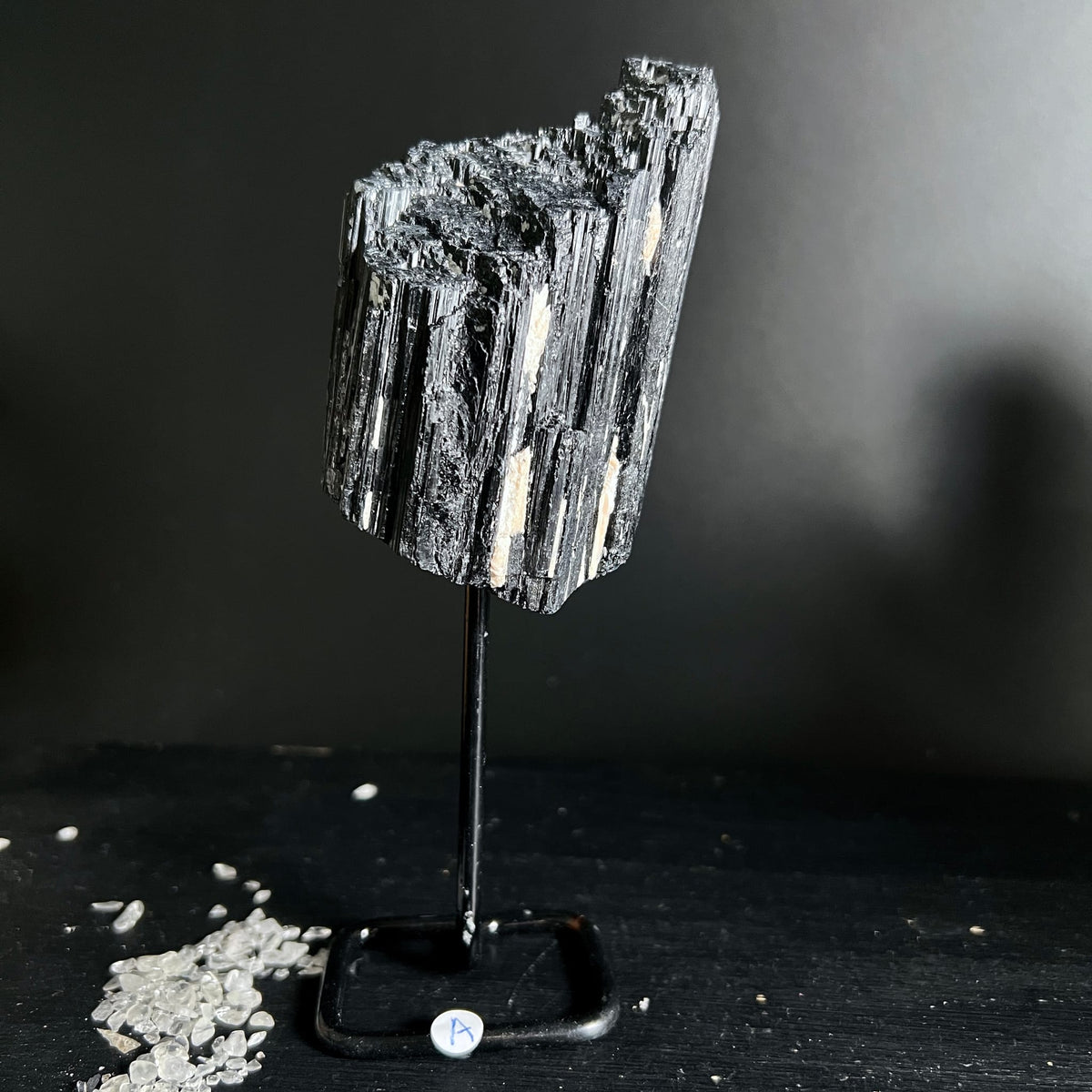 Schwarzer Turmalin Rohstein mit parallelen Kristallstäben, silbrig glänzend, auf schwarzem Metallständer | Happy Minerals