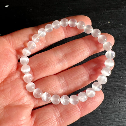 Selenit Armband mit milchig-transluzenten Perlen, zartes Cat's-Eye-Lichtband sichtbar, an Hand gehalten | Happy Minerals