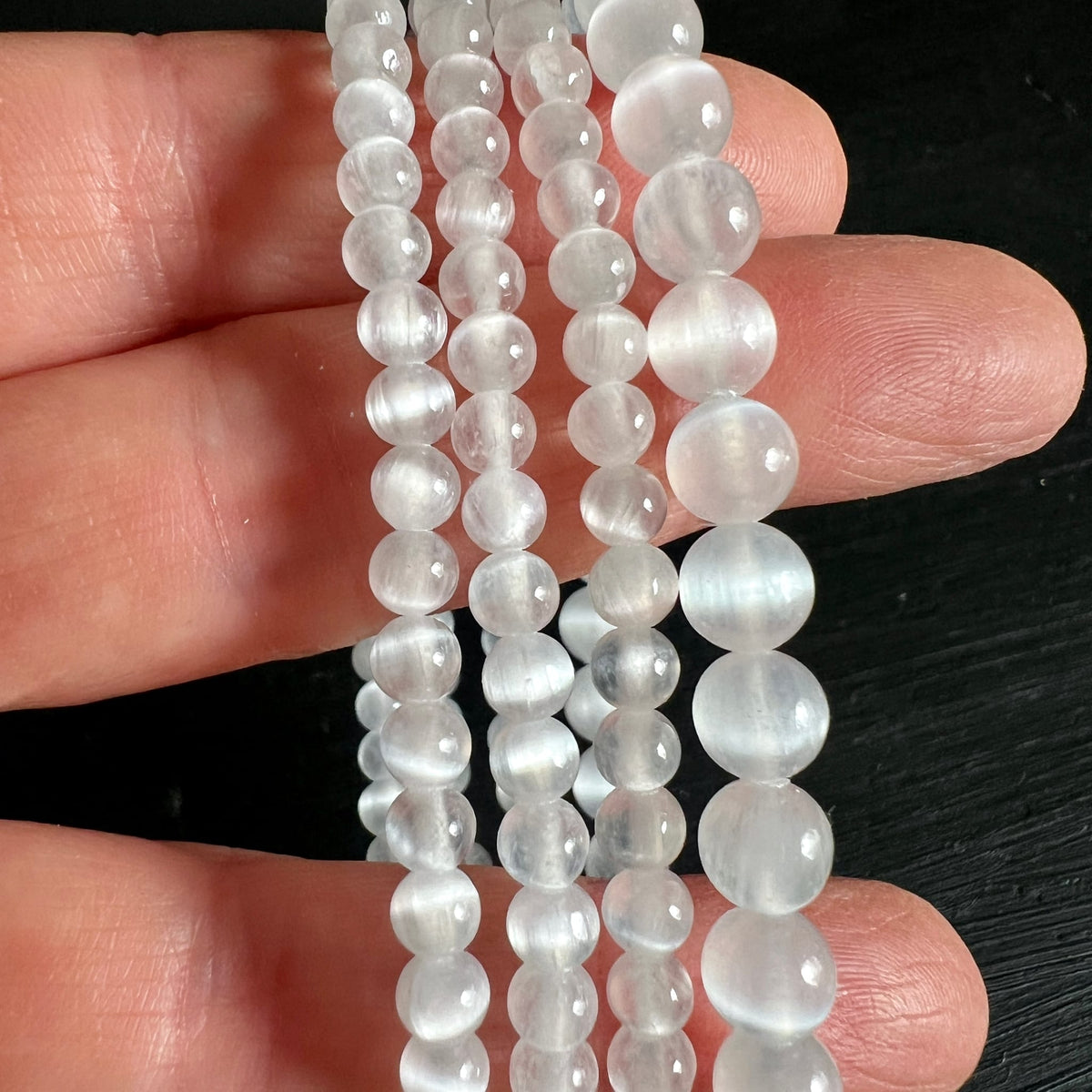 Selenit Armband aus milchig-transparenten Perlen 4-6mm mit feinen Glanzstreifen, auf Fingern drapiert | Happy Minerals
